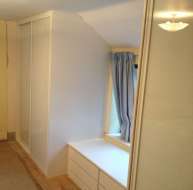 Plain white doors with white frames in the eaves, with a chest of drawers below the window